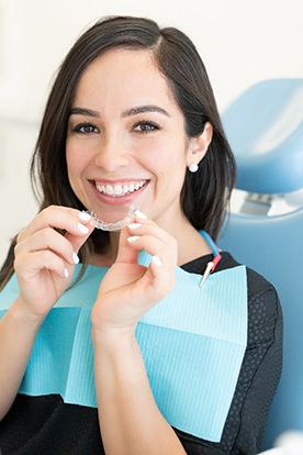 Smiling woman in dental chair holding clear aligners