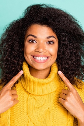 Woman in yellow sweater pointing to her smile