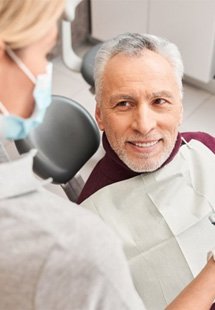 Senior dental patient in dental chair talking to dental team member