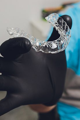 Dentist holding a clear aligner with black gloves