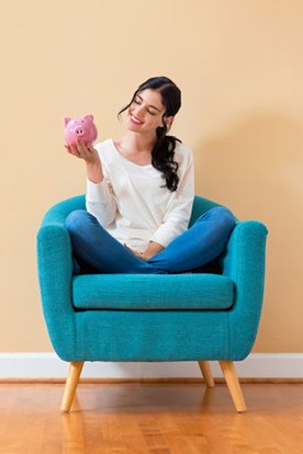 Woman sitting in a cozy chair and smiling at her piggy bank