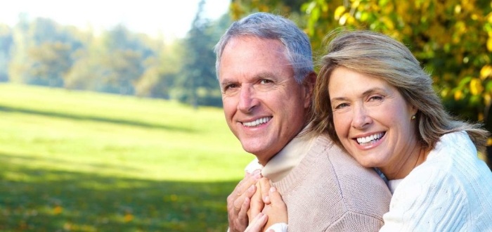 Man and woman grinning outdoors with dental crowns and bridges