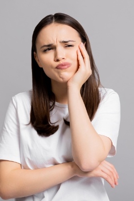 Woman in white T shirt holding her cheek in pain