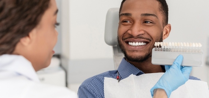 Man's smile compared to dental restoration color options while receiving dental services