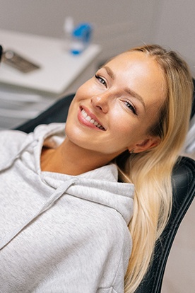 Woman in gray sweatshirt smiling while sitting in treatment chair